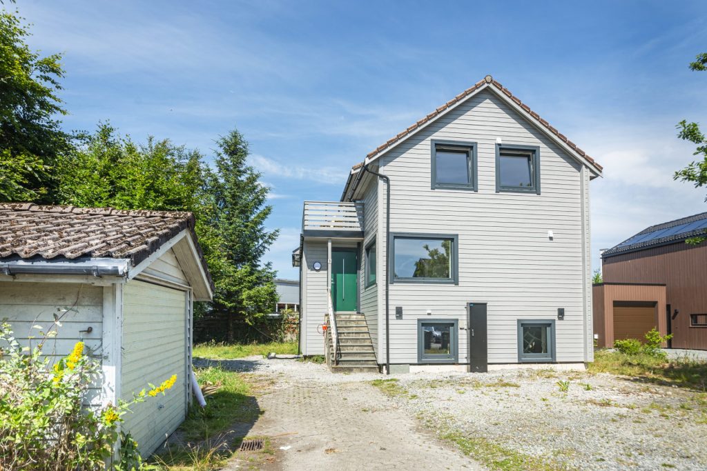 Hvitmalt enebolig med grønn inngangsdør fotografert i sollys